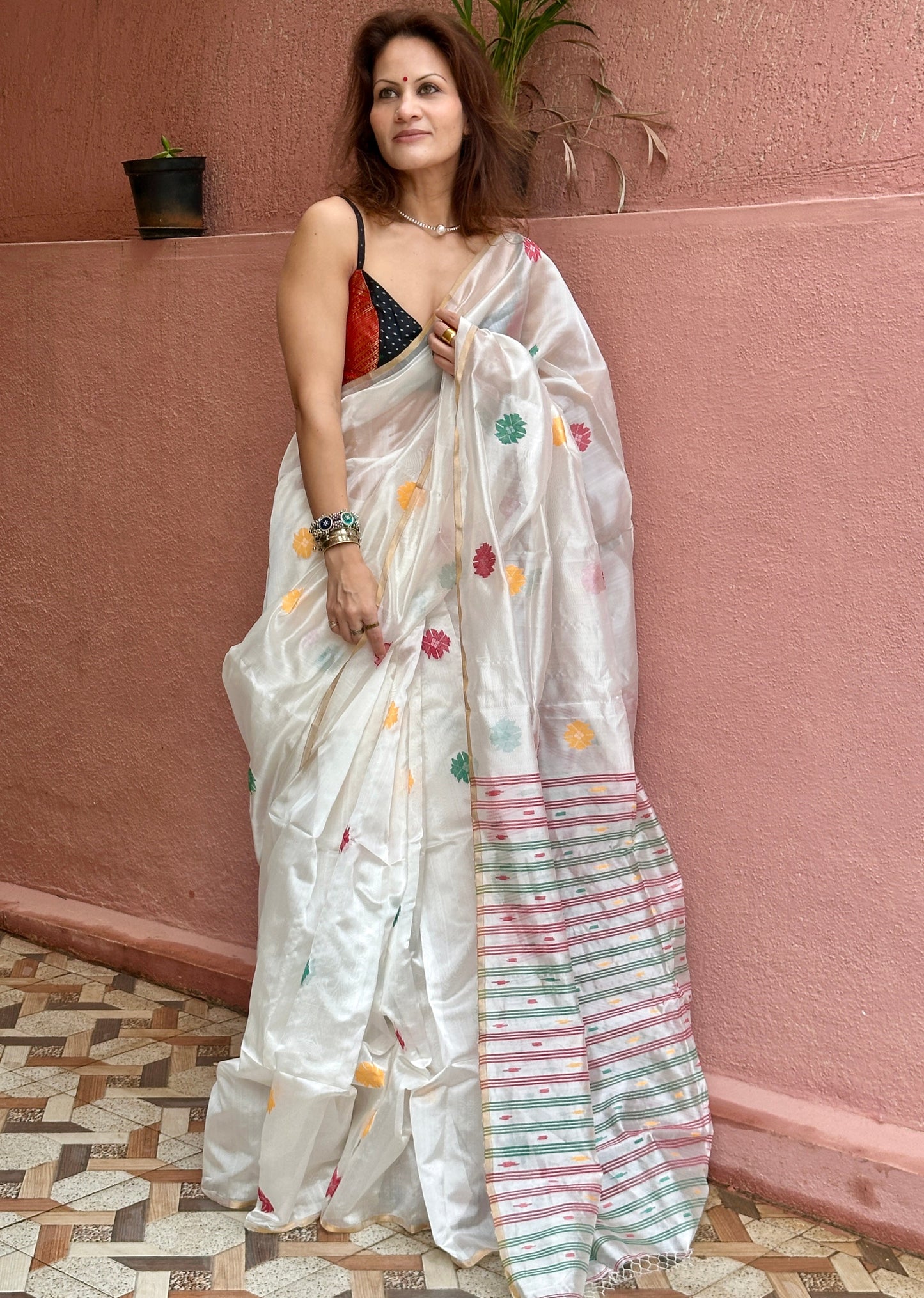 Woman wearing a white saree with colorful patterns against a pink wall.