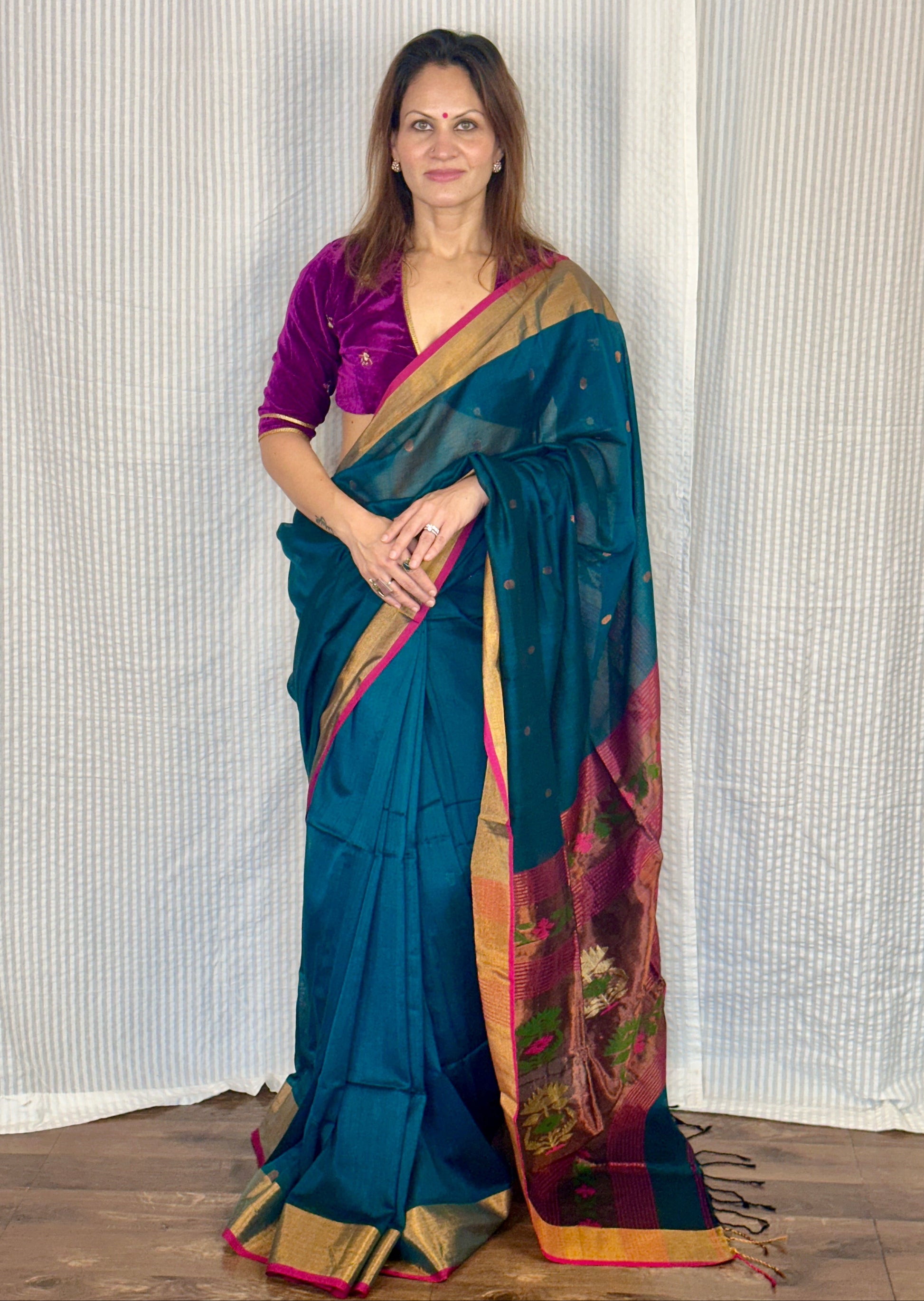 Woman wearing a green saree with a colorful border against a white curtain background
